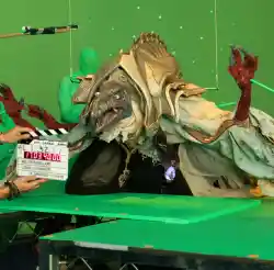 Una enorme marioneta delante de un chroma, siendo manejada por varios profesionales